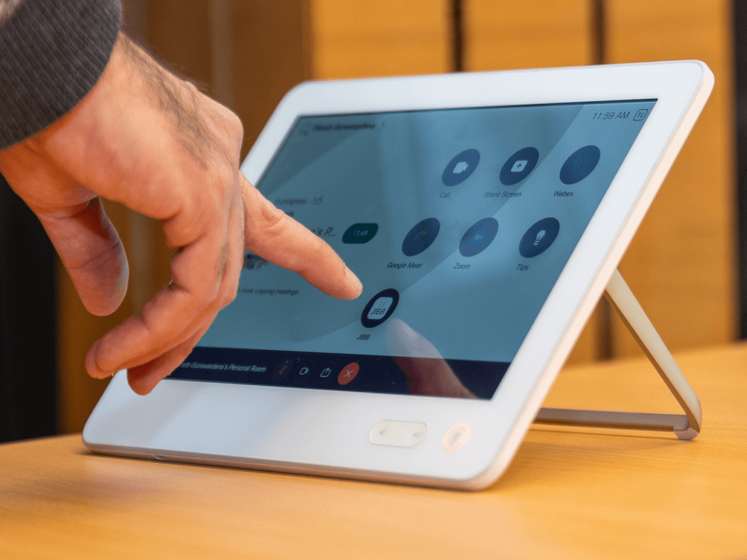 Hand interacting with a white touchscreen device displaying video conference app icons including Call, Share Screen, Webex, Google Meet, Zoom, and JIBB.