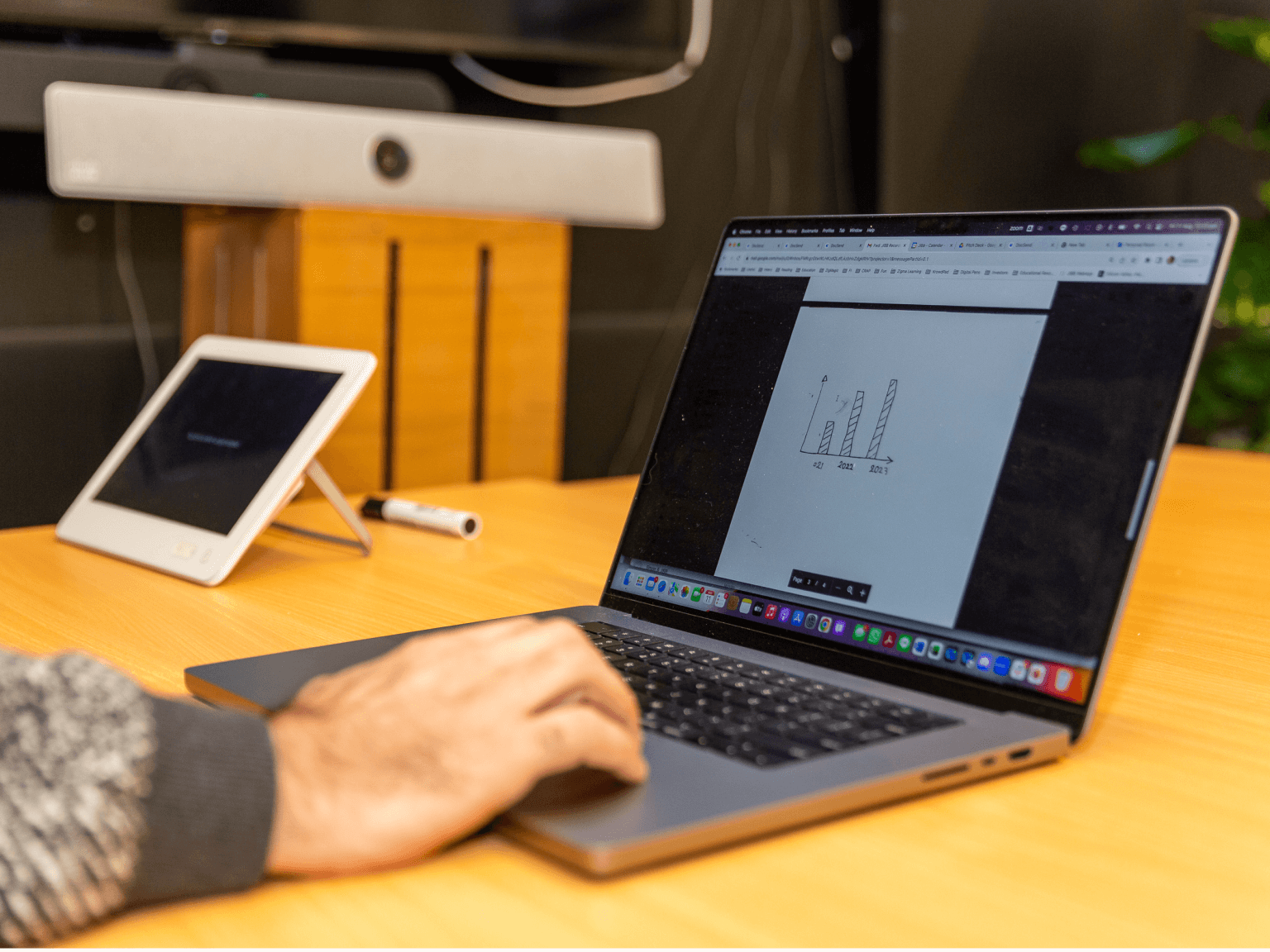 Person using a laptop displaying a bar chart with data for 2021, 2022, and 2023 on a wooden table.