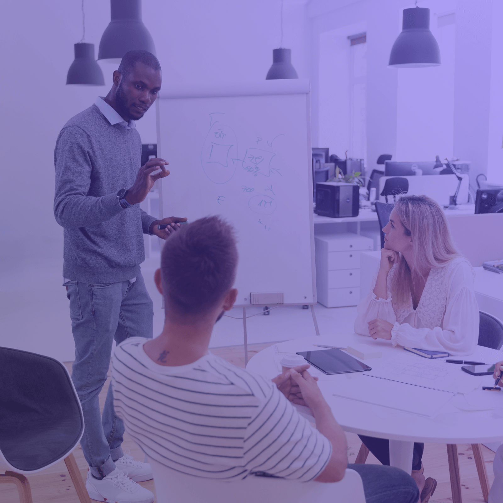 Man presenting ideas at whiteboard to two seated colleagues in a modern office meeting.
