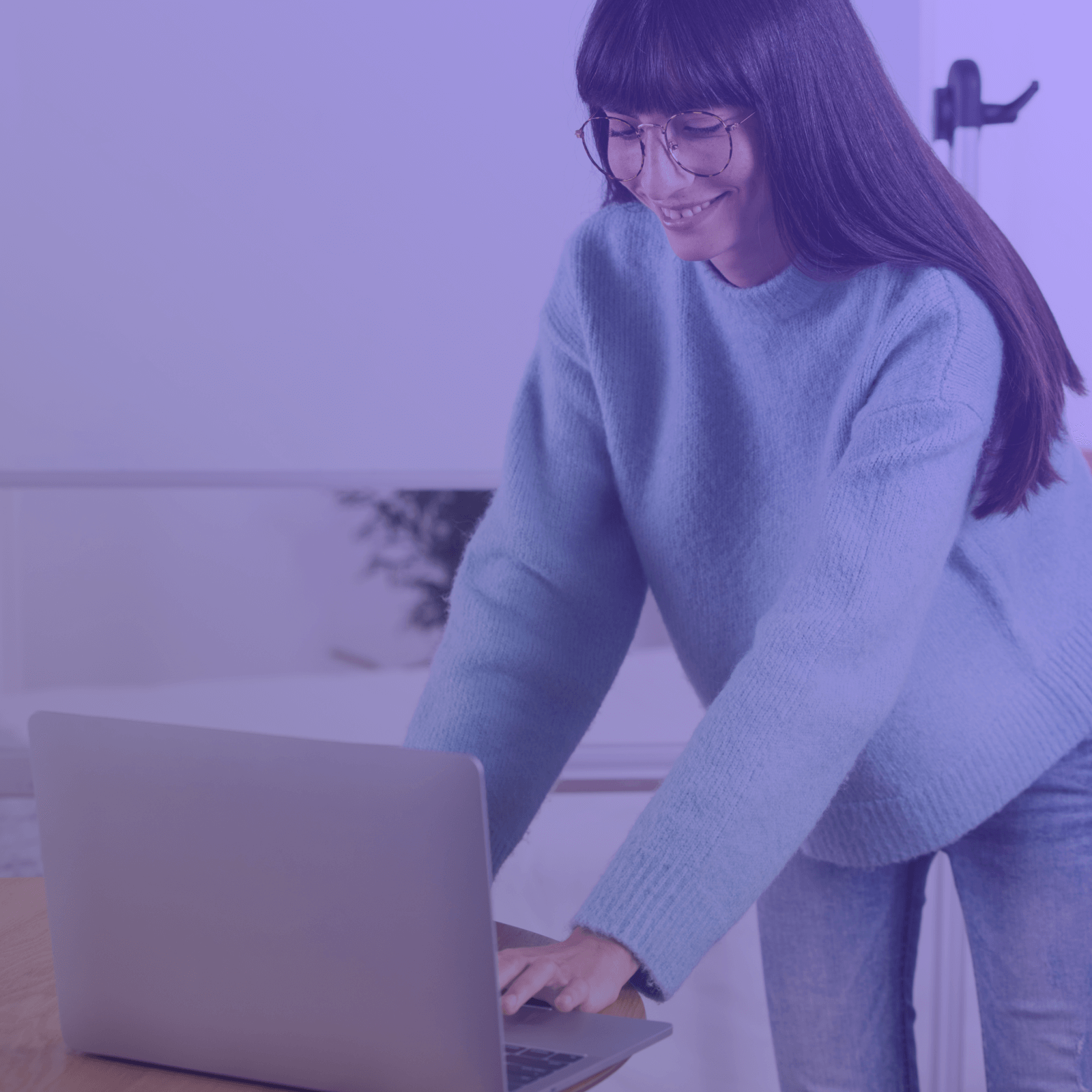 Smiling woman with glasses and long hair working on a laptop while standing.