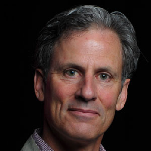 Headshot of a middle-aged man with gray hair against a black background.