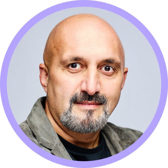 Portrait of a bald man with a short gray beard wearing a gray jacket and black shirt, on a light blue background with a purple circular border.
