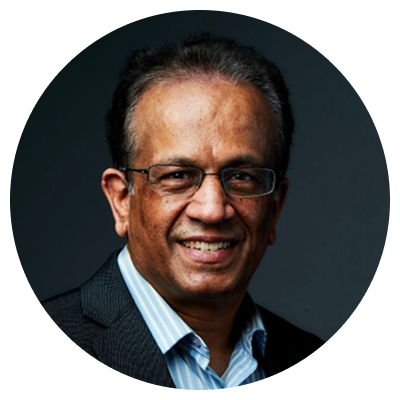 Smiling middle-aged man with glasses wearing a dark blazer and blue striped shirt against a dark background.